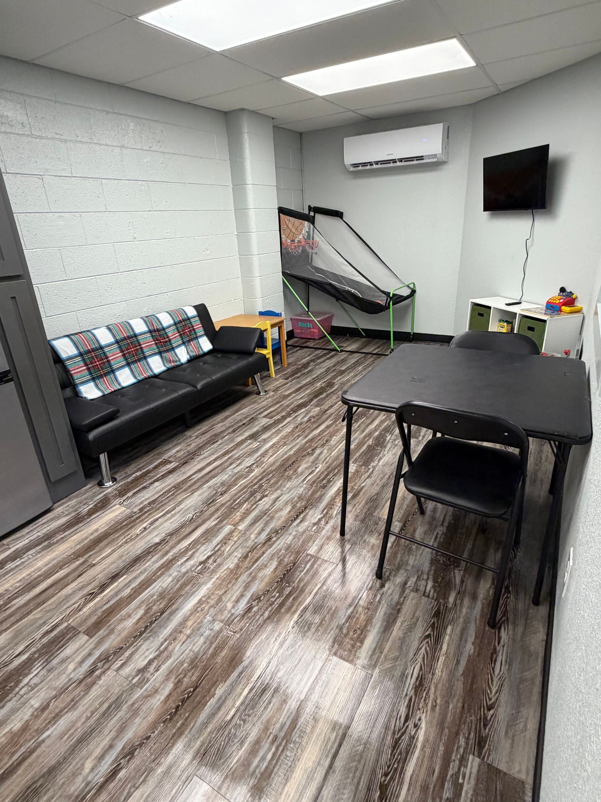 Room with black couch, table, and game in a facility with wood-look flooring.