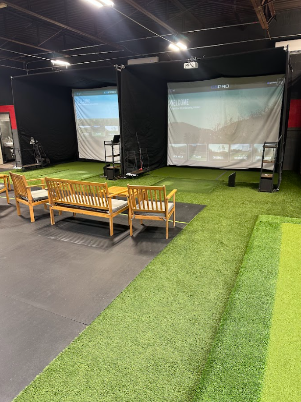 Indoor golf simulator bays with screens, turf flooring, and seating.