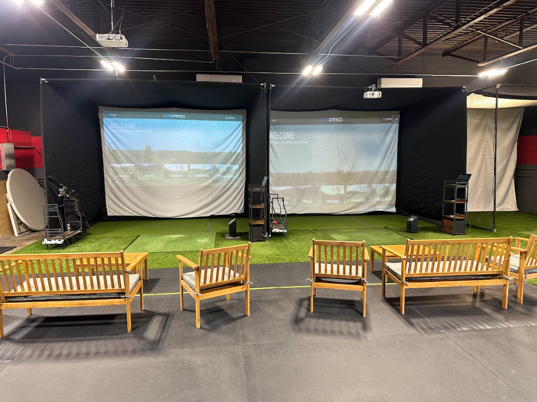 Indoor golf simulator bays with screens, turf, seating, and equipment.