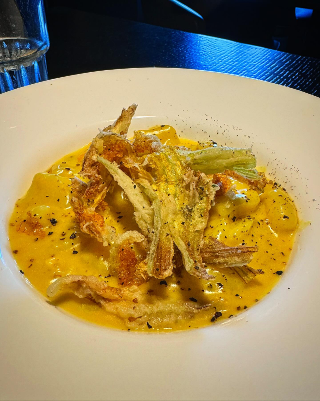 Un cremoso piatto di pasta condito con pesce sminuzzato, servito su un piatto bianco in un ristorante dall'atmosfera soffusa.