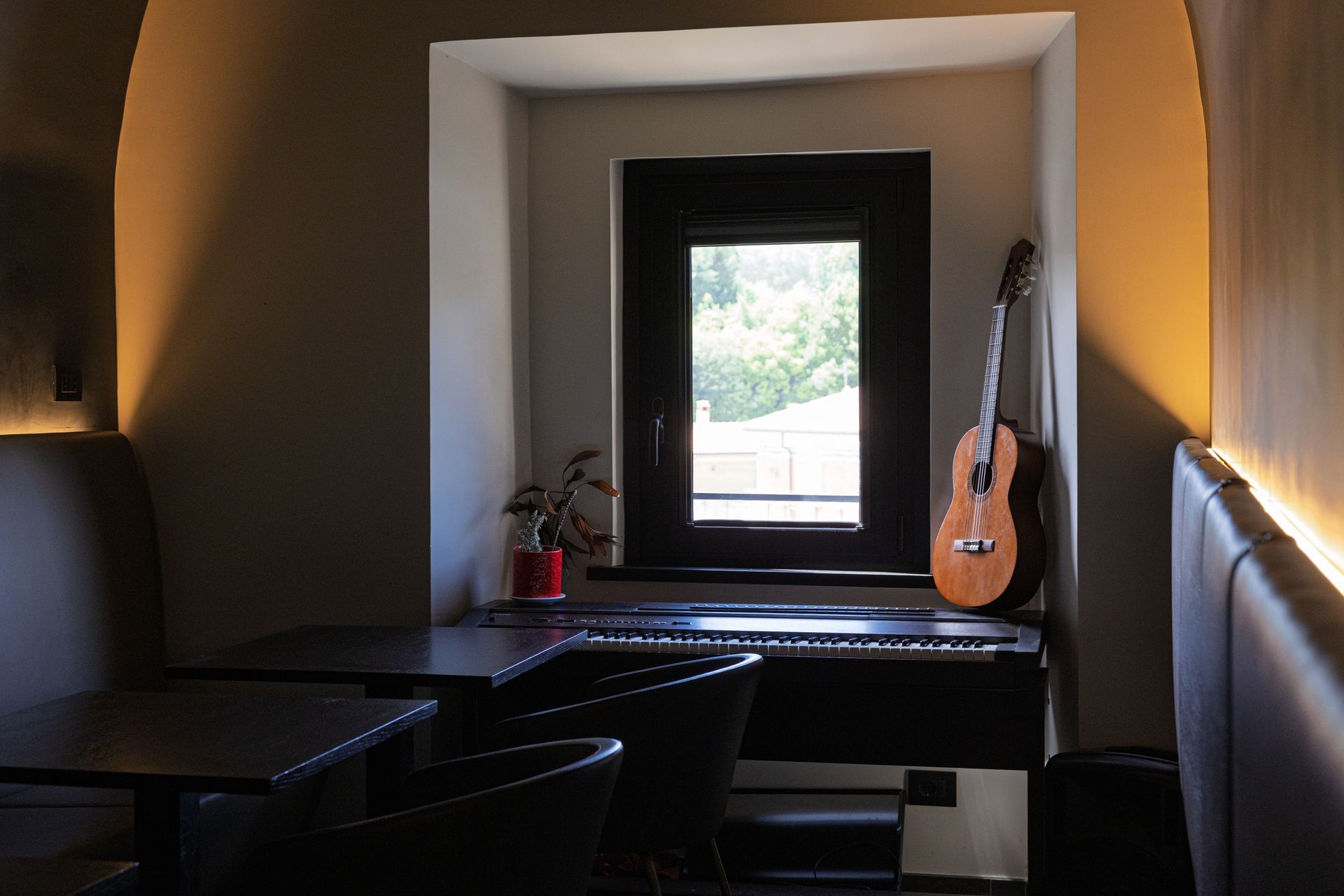 Una stanza accogliente con un angolo finestrato, una chitarra e un tavolo, illuminata da calde applique a parete.