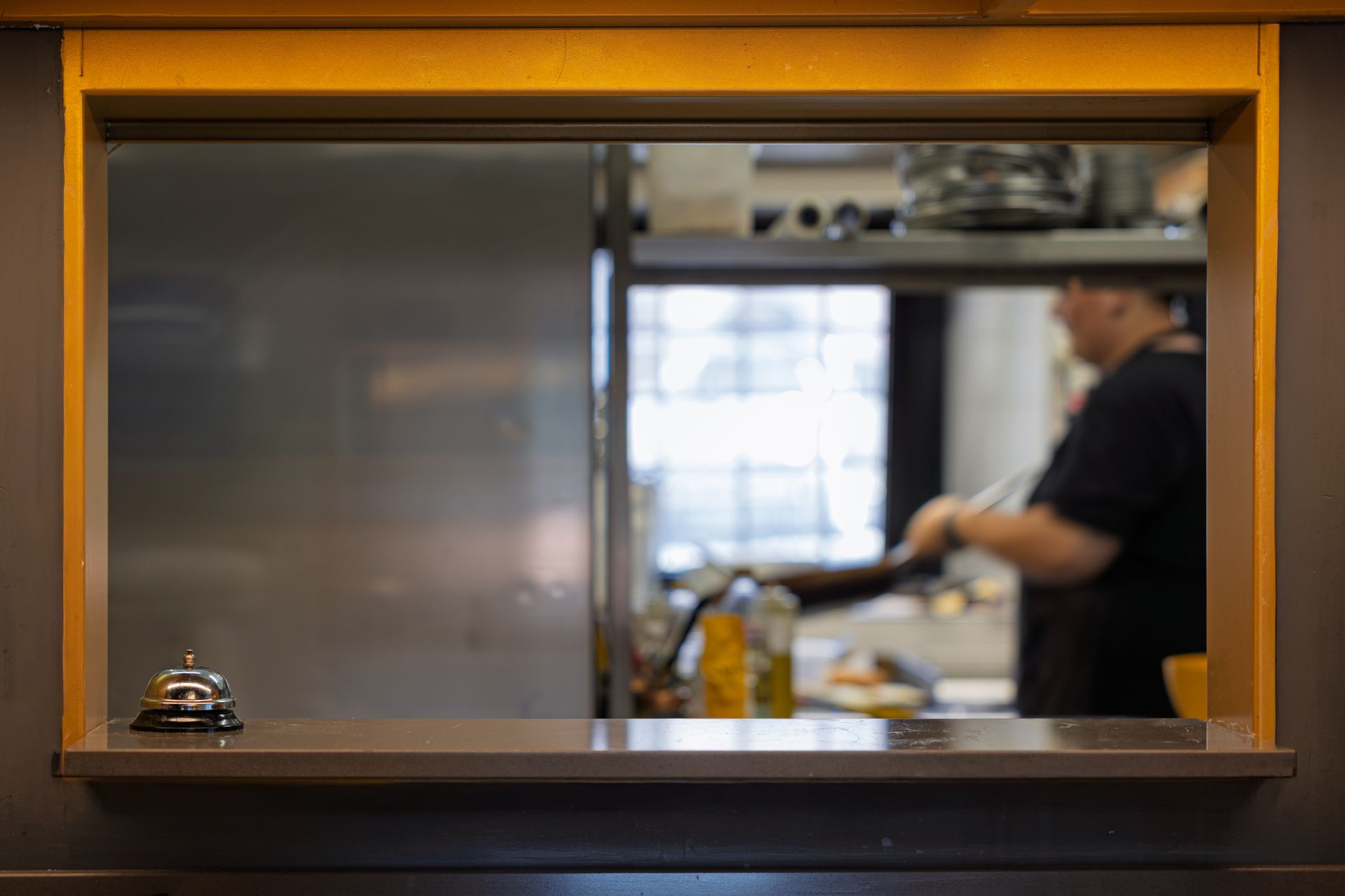 Finestra passavivande della cucina di un ristorante con un campanello e uno chef sfocato sullo sfondo.