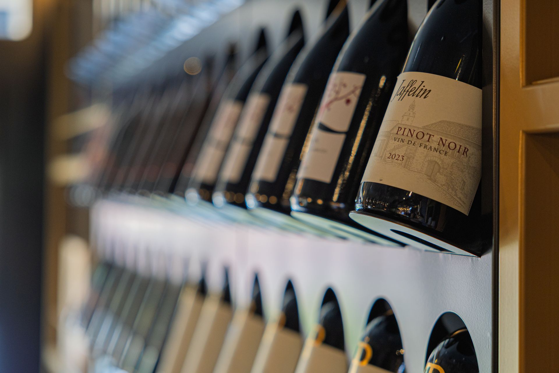 File di bottiglie di vino esposte su scaffali inclinati in un negozio, con le etichette rivolte verso l'esterno.