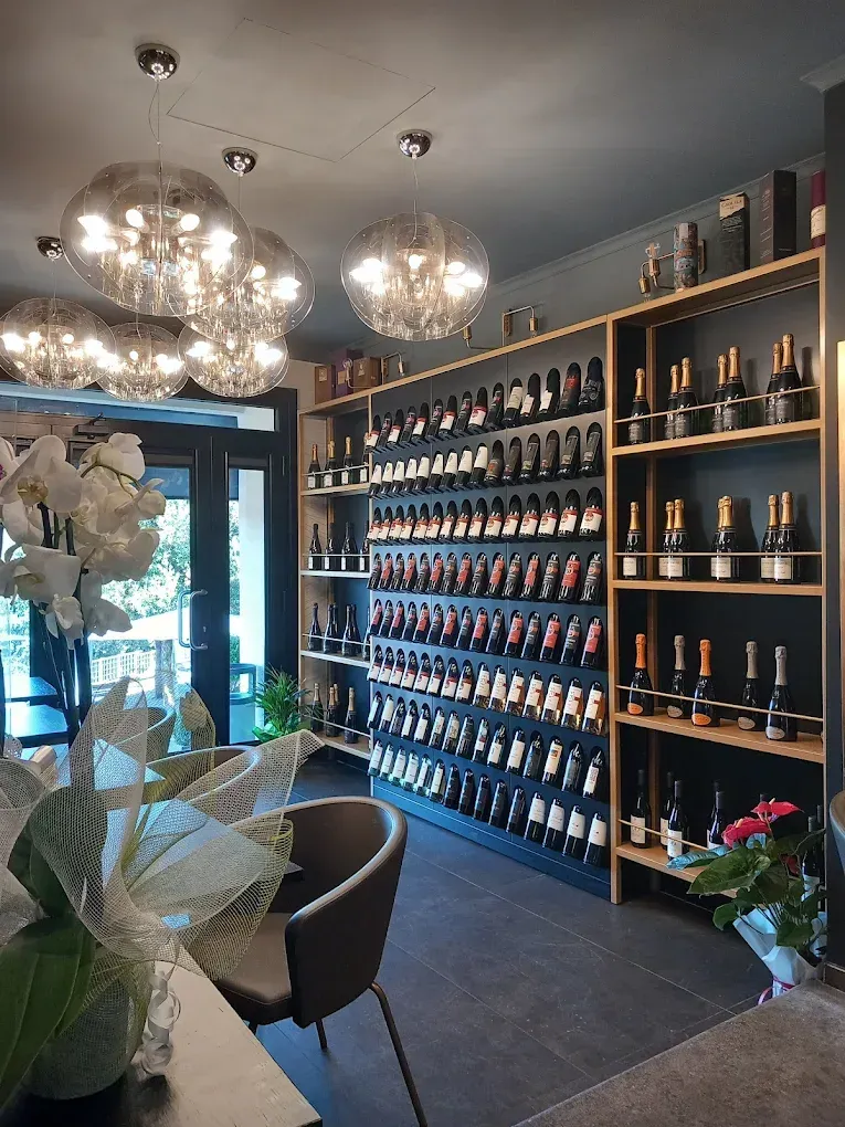 Elegante interno di un'enoteca con scaffali di bottiglie, lampadari e una porta a vetri all'ingresso.
