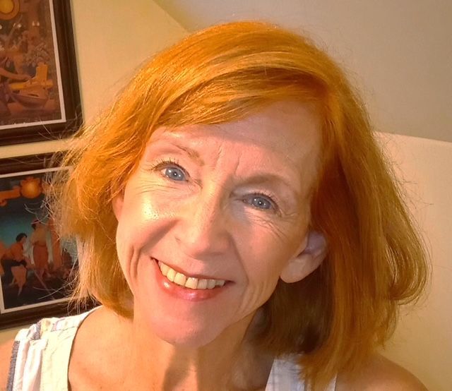 Woman with red hair smiling, blue eyes, fair skin; paintings in the background.
