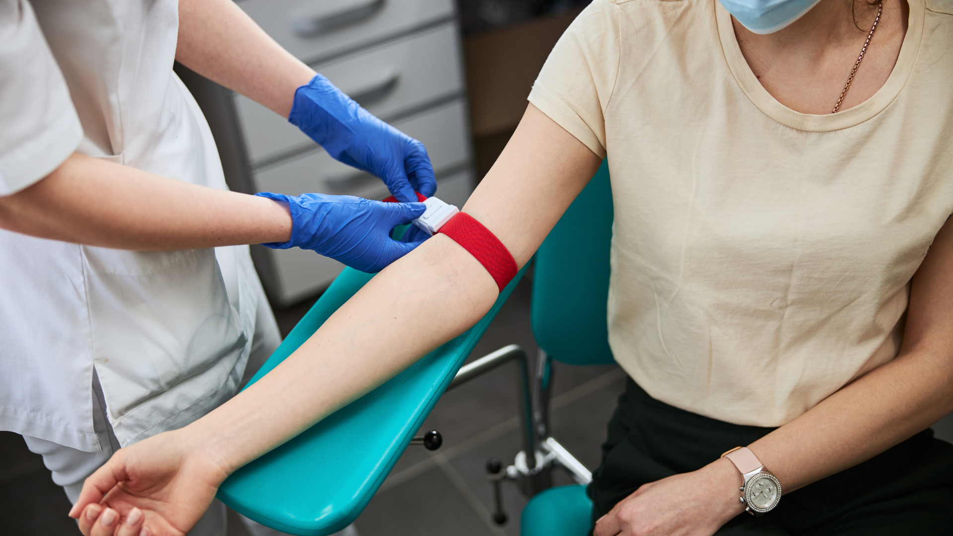 A woman sits in a medical chair as a doctor draws blood from her arm in a clinical setting.