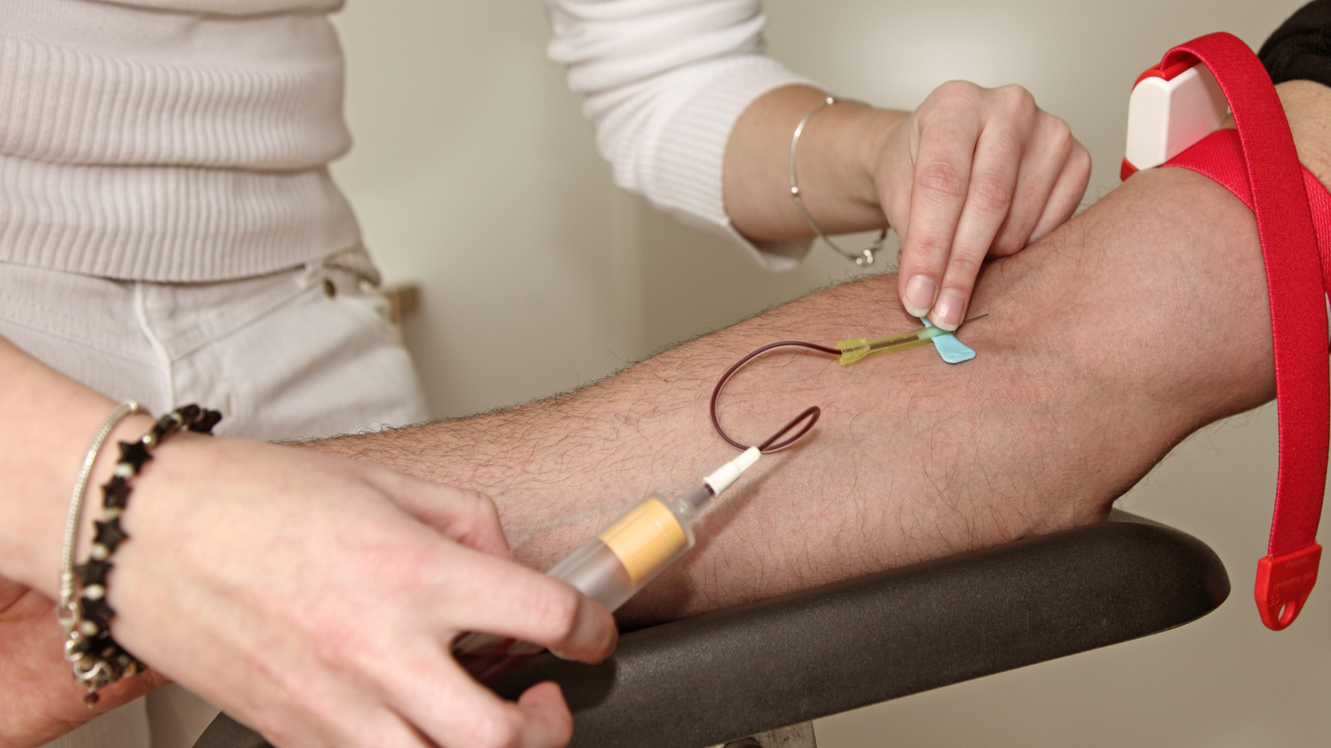 A healthcare professional draws blood from a patient's arm in a clinical setting.