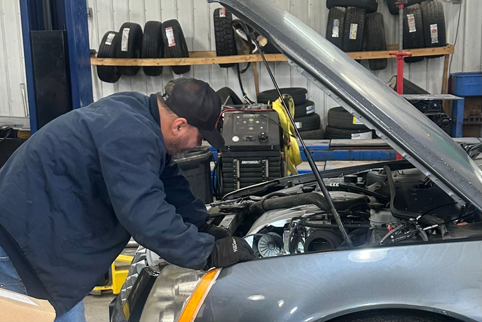 Mechanic working on car engine in a garage. Wearing black hat and gloves, car hood open. | Gentleman’s Garage