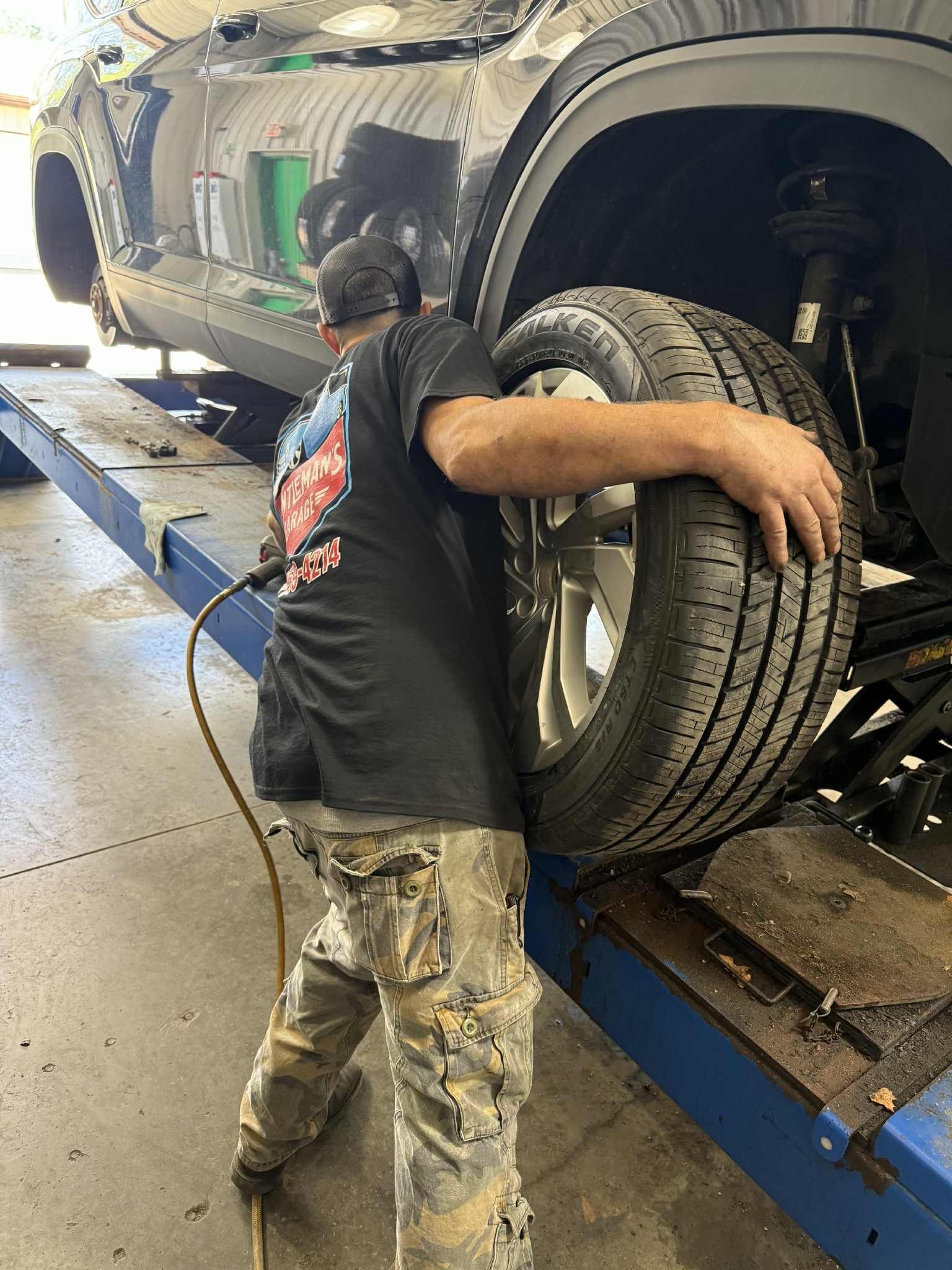 Mechanic holding a tire while working on a car on a lift. Shop interior. | Gentleman’s Garage