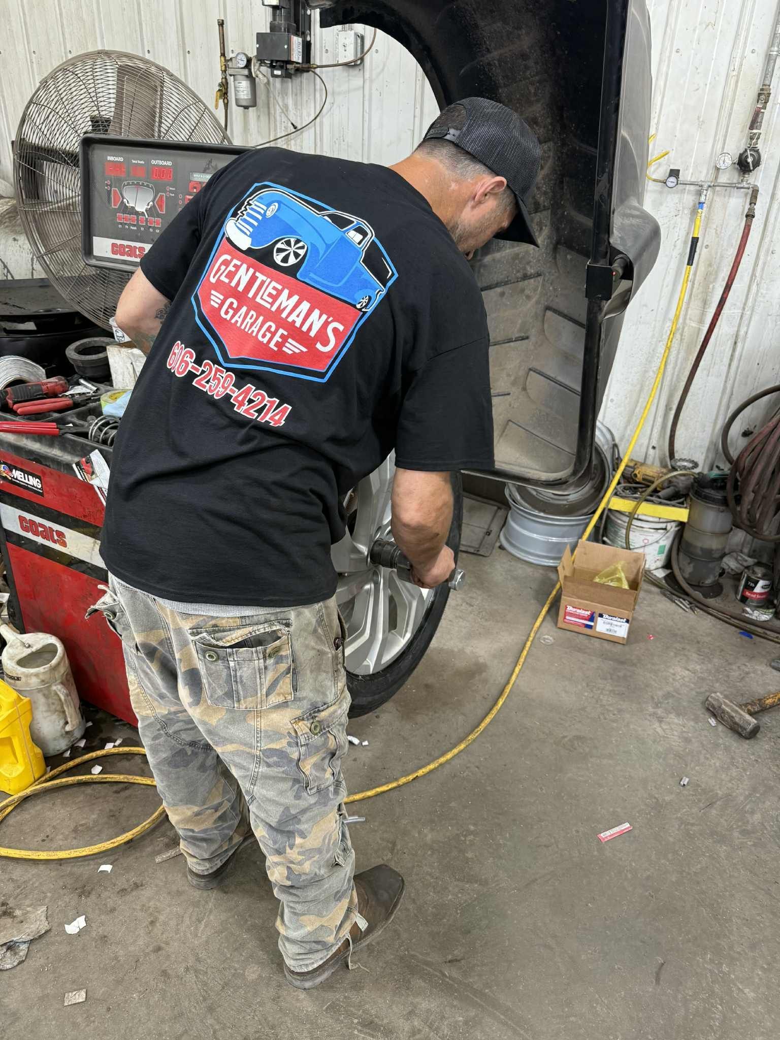Mechanic in a black shirt working on a tire in a garage, using a tool. | Gentleman’s Garage
