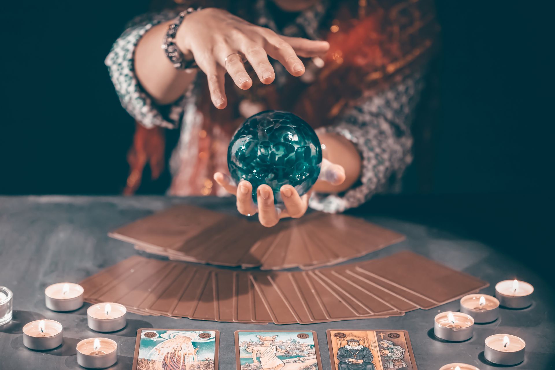 Fortune teller with tarot cards on table near burning candles