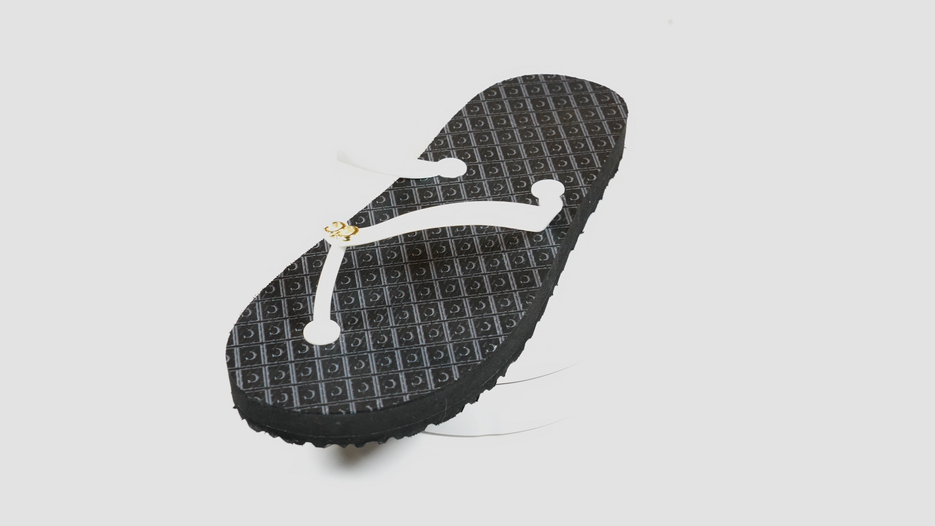A black flip flop is sitting on a white surface.