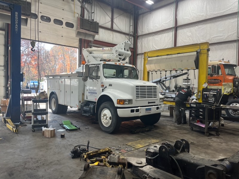 A white truck is parked in a garage with a man working on it.
