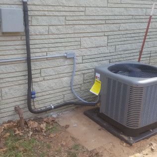An air conditioning unit outside a brick building. Electrical conduit and a gray box are visible.