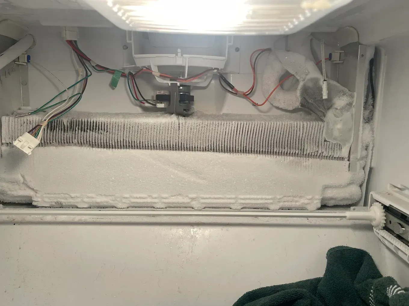 Inside of a freezer, heavily frosted with ice buildup. Wires and a fan are visible above the ice.