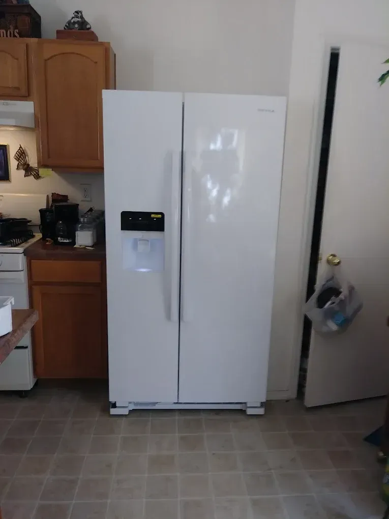 White side-by-side refrigerator in a kitchen. Adjacent cabinets and doorway visible.