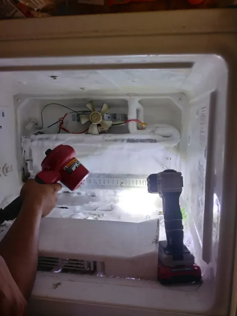 Person defrosting a freezer with a red heat gun and a flashlight. White ice is inside the freezer.