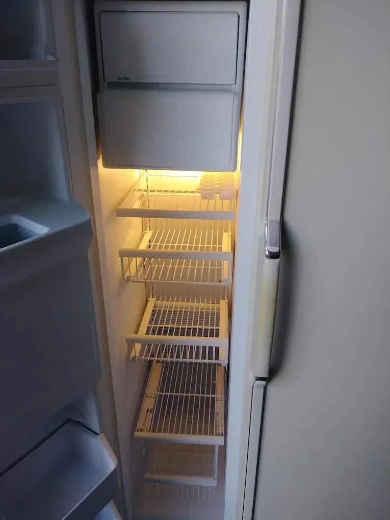 Interior of a refrigerator with bright light, empty shelves, and a freezer compartment.