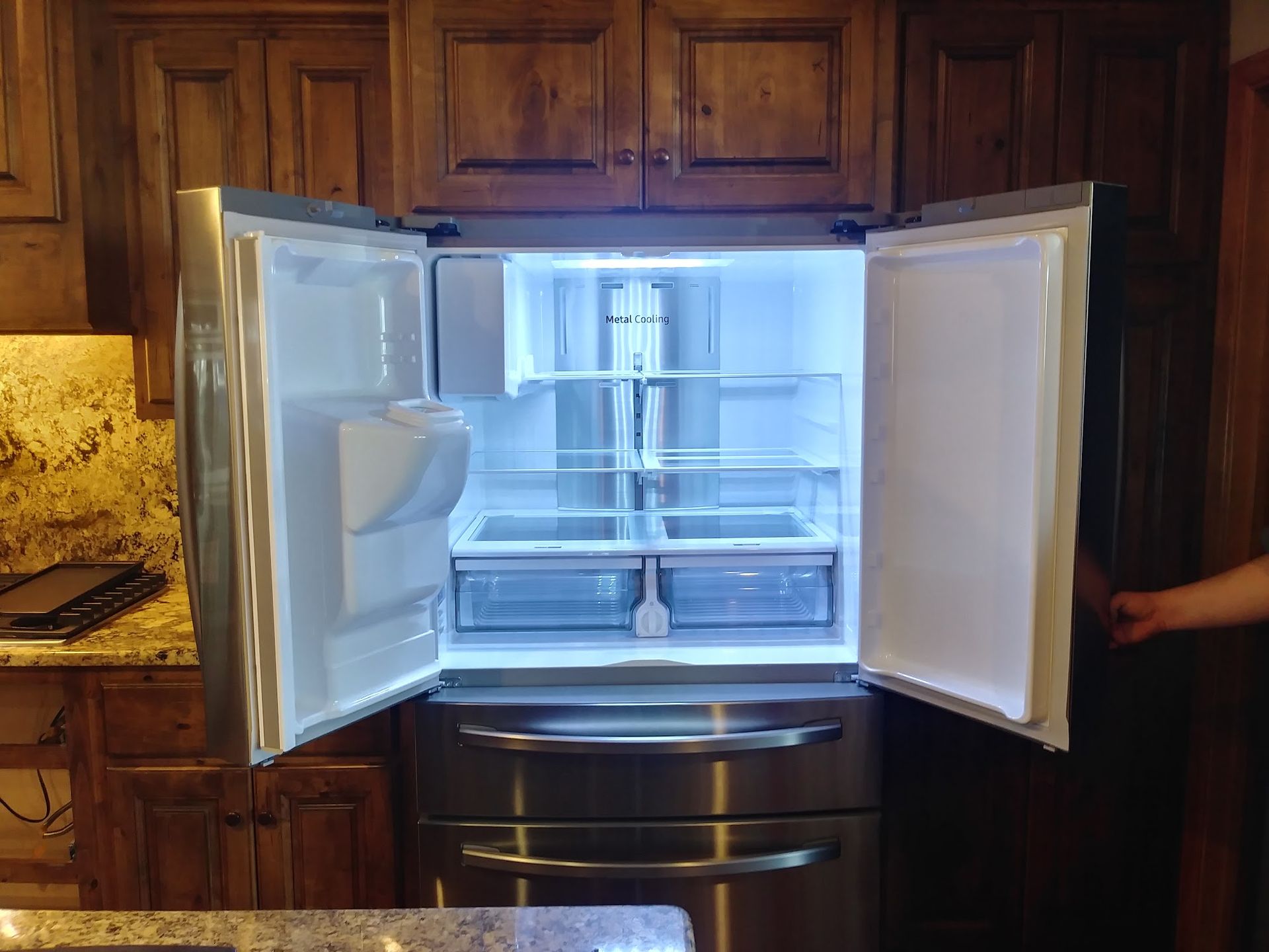 Open stainless steel refrigerator in kitchen with wooden cabinets.