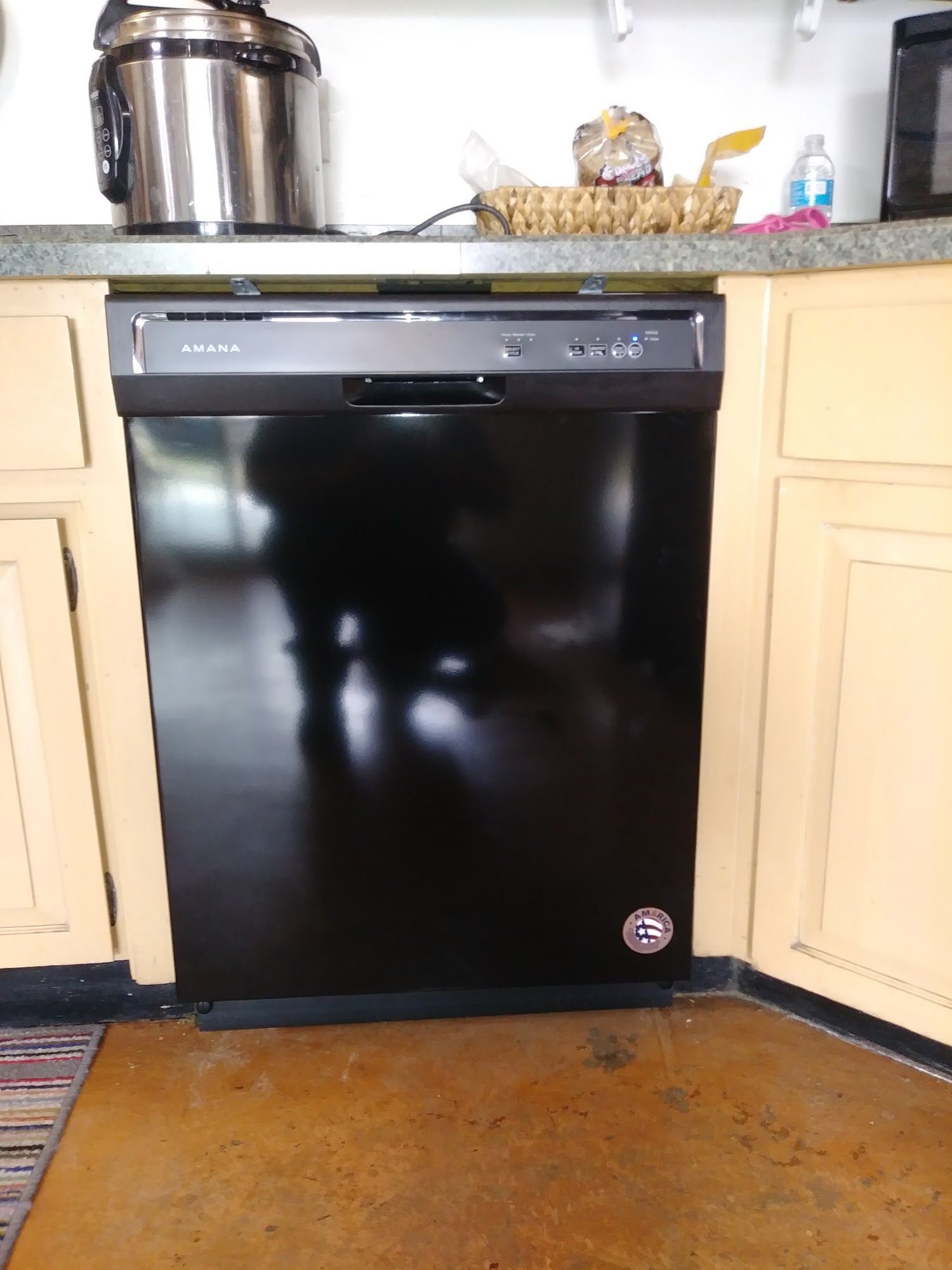 Black Amana dishwasher in a kitchen, with yellow cabinets and a stainless steel rice cooker on the counter.