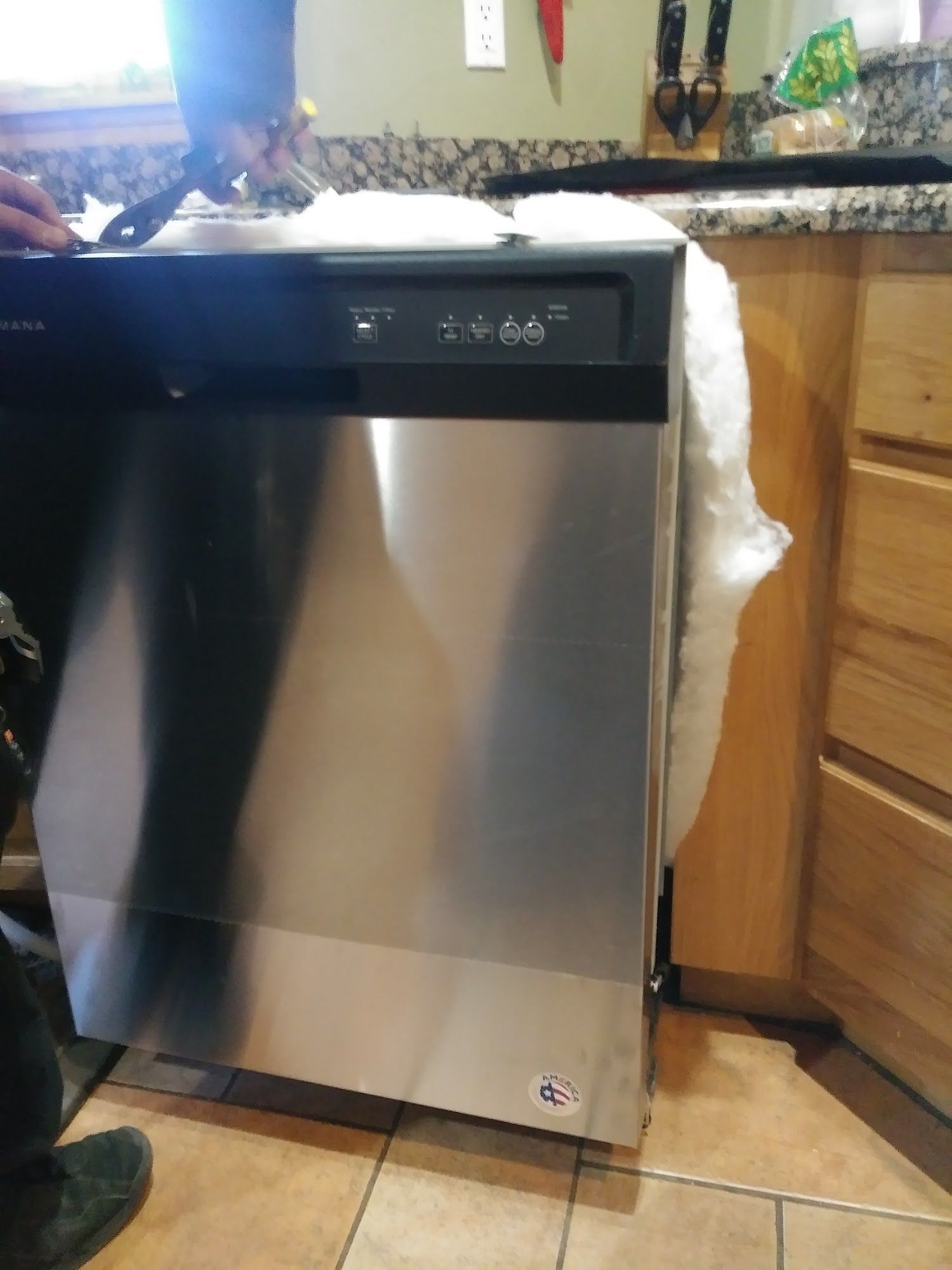 Stainless steel dishwasher being installed in a kitchen, next to wooden cabinets.
