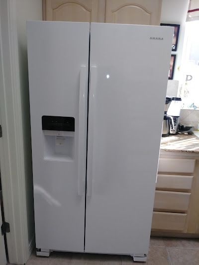 White side-by-side refrigerator with water/ice dispenser, in a kitchen setting.