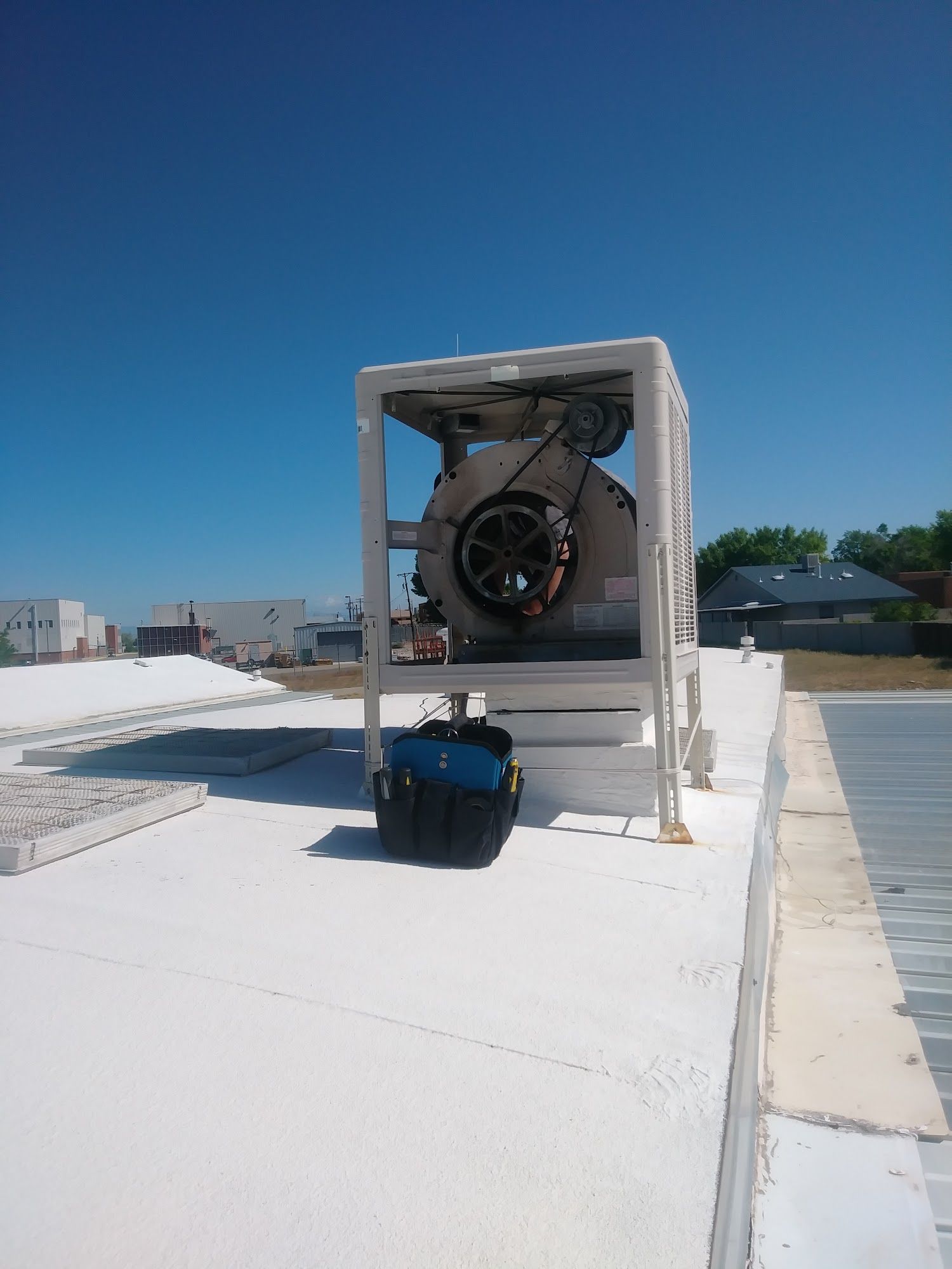 Rooftop HVAC unit with visible fan and toolbox on white surface against blue sky.