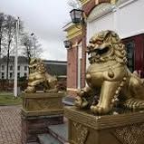Twee gouden leeuwenbeelden op sokkels buiten een gebouwingang.