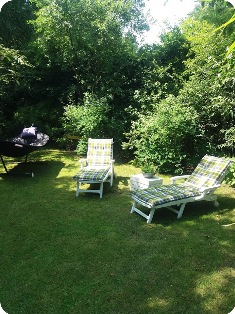 Twee gestreepte loungestoelen op een grasveld onder dichte groene bomen in een zonnige tuin.