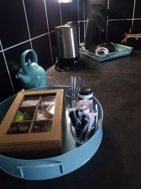 Een blauw dienblad met theebenodigdheden, een houten doos en een glazen pot op een donkere tafel.