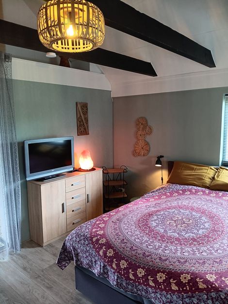 Gezellige slaapkamer met een bedsprei met patroon, een commode, een lamp, wanddecoratie en zichtbare donkere plafondbalken.