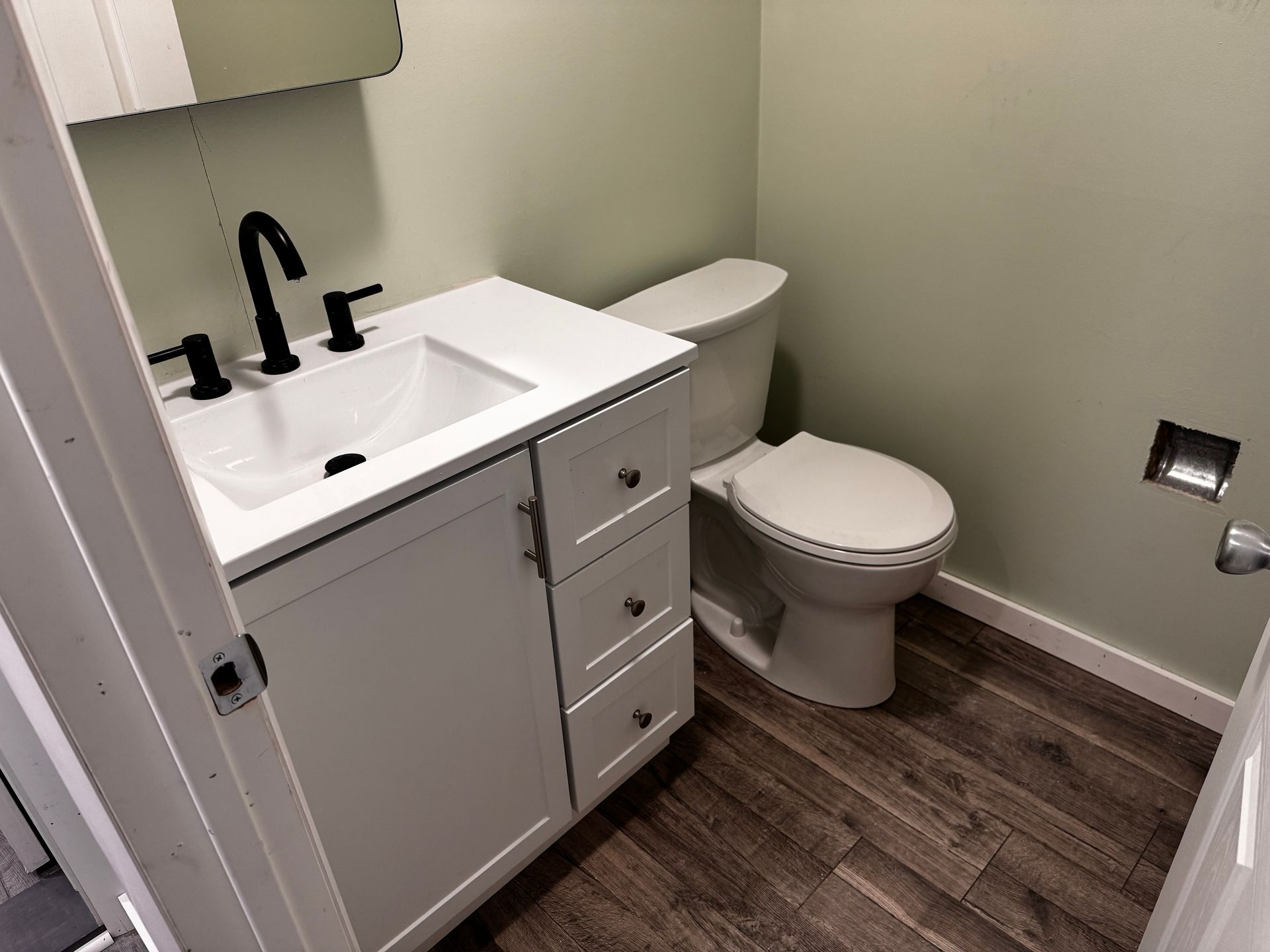 Bathroom with white vanity, black faucet, toilet, and wood-look flooring.