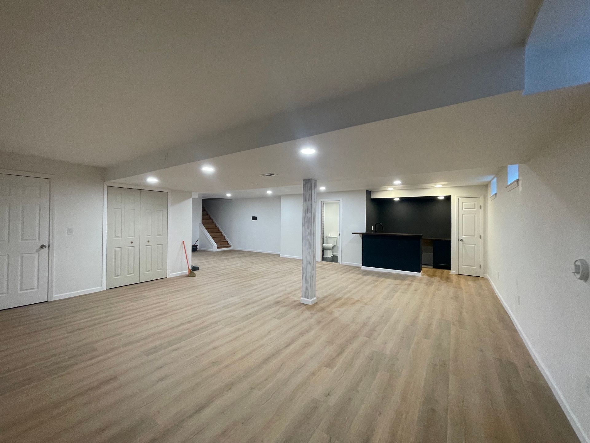 Empty basement with wood-look flooring, white walls, built-in bar, and a central support column.