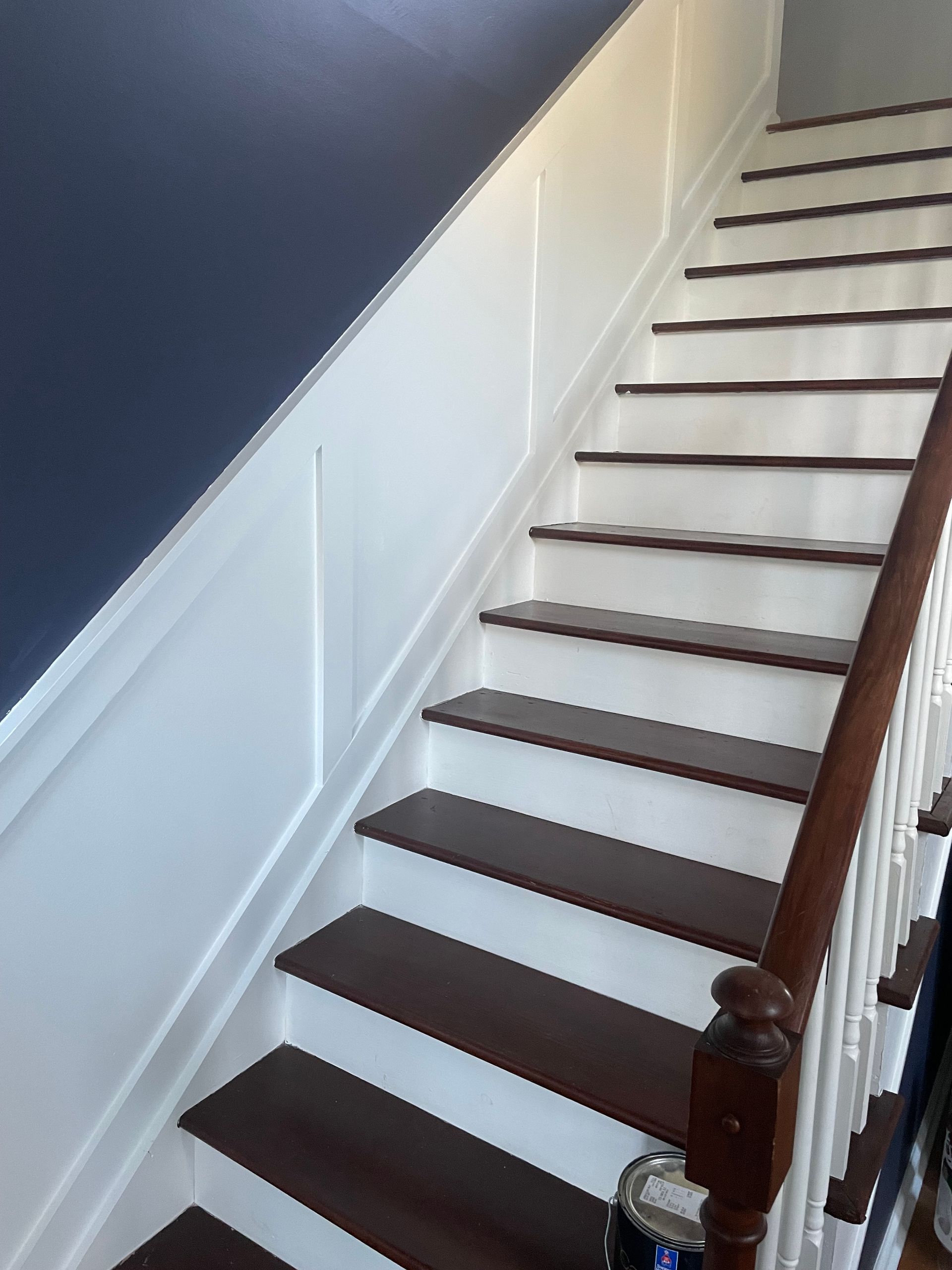Staircase with white risers and dark treads, white paneling on a navy blue wall, and a wooden railing.