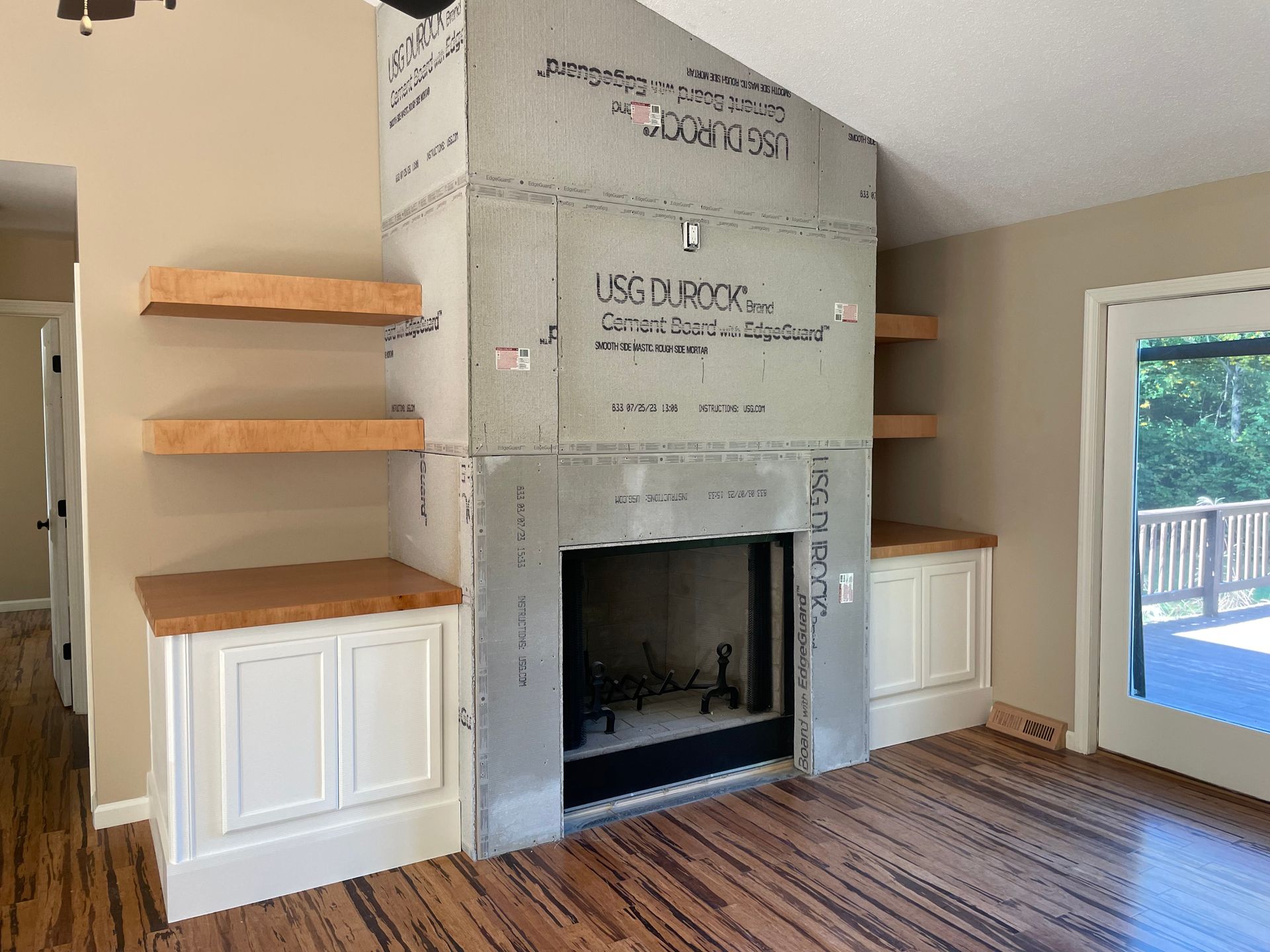 Fireplace under construction, with shelves and cabinets; wood floors and tan walls.