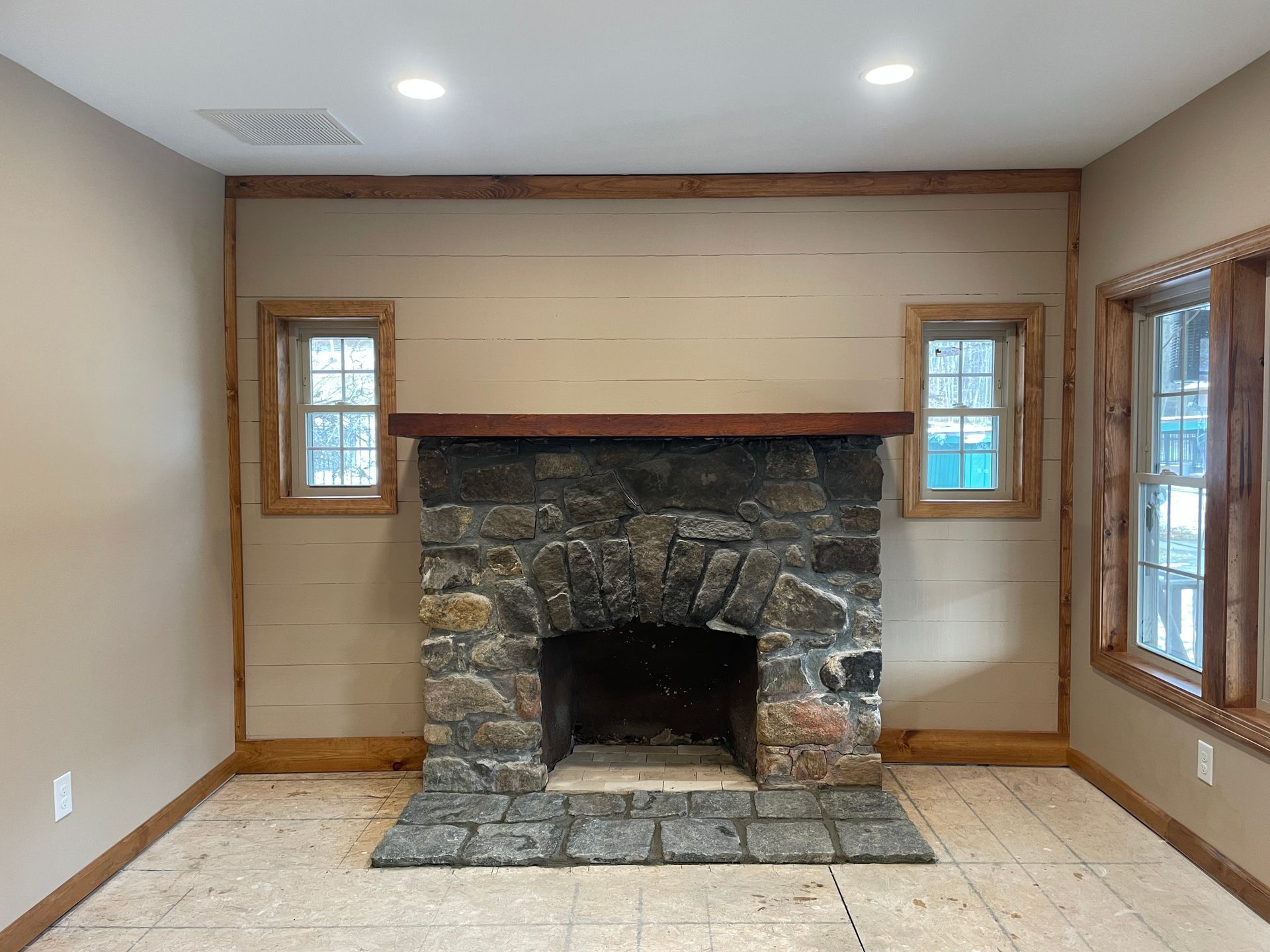 Stone fireplace centered between two windows on a beige wall, wooden trim.