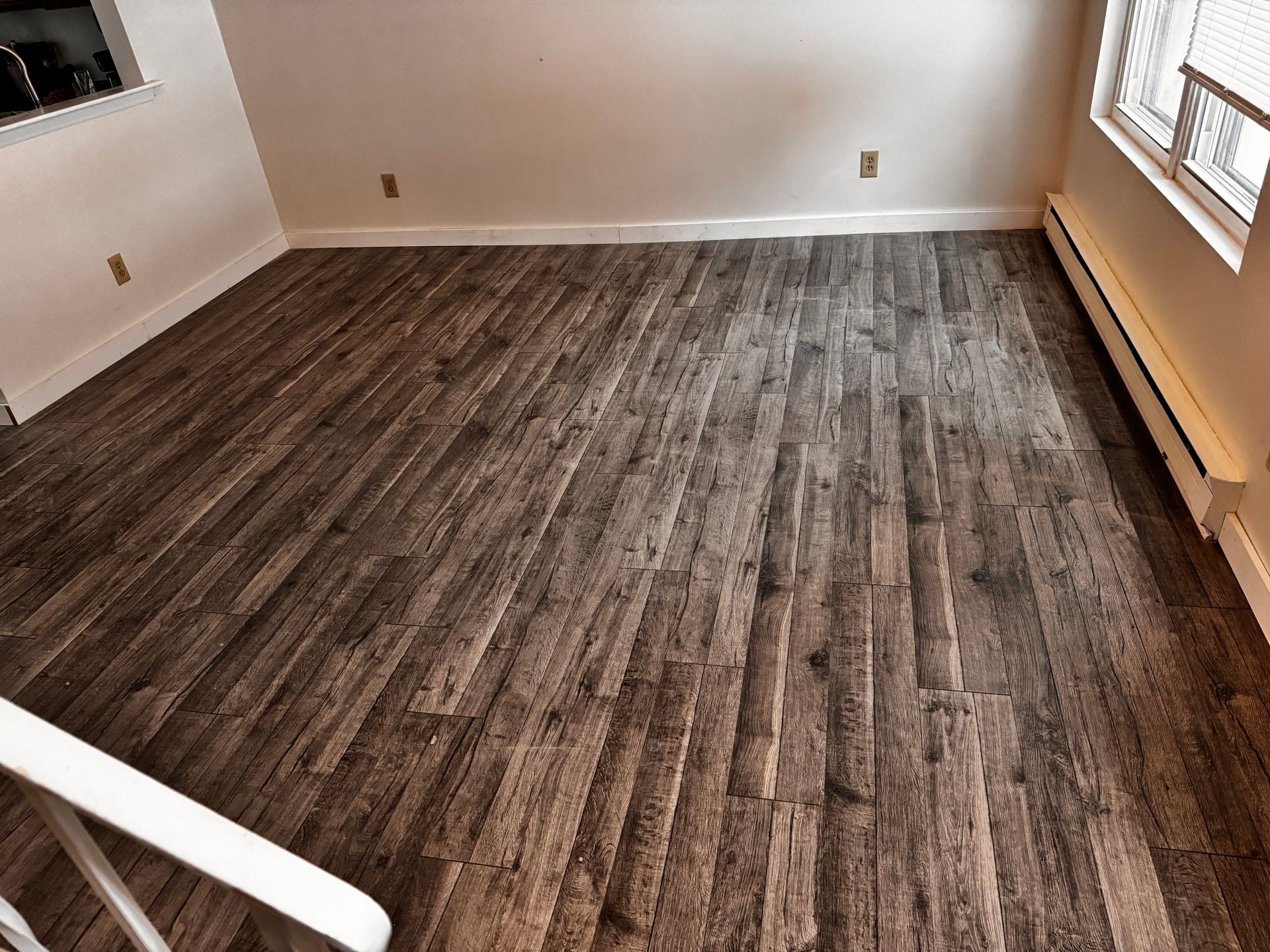 Empty room with wood-look flooring, white walls, and a small window with blinds.