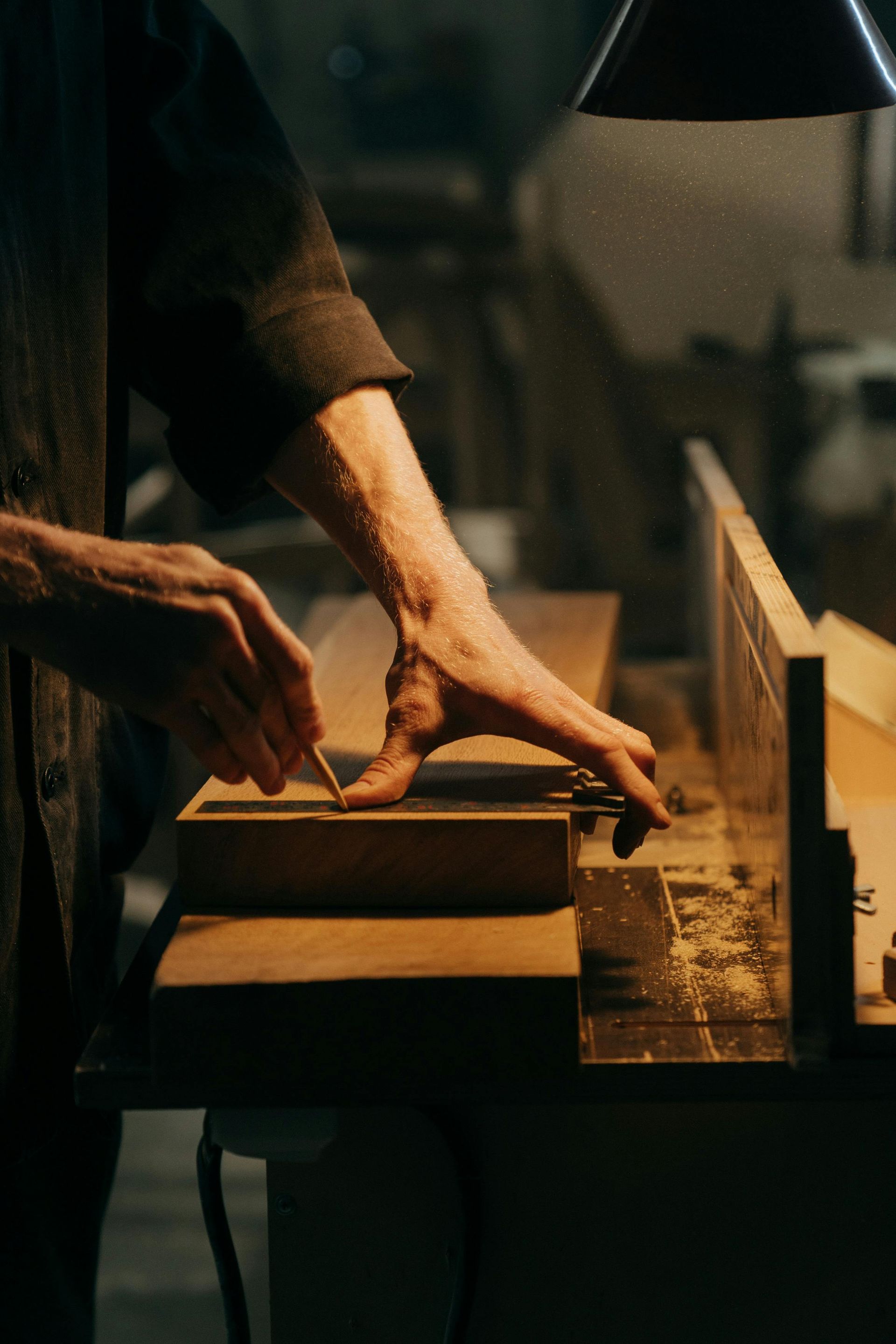A carpenter using a tool to work on wood in a dimly lit workshop.