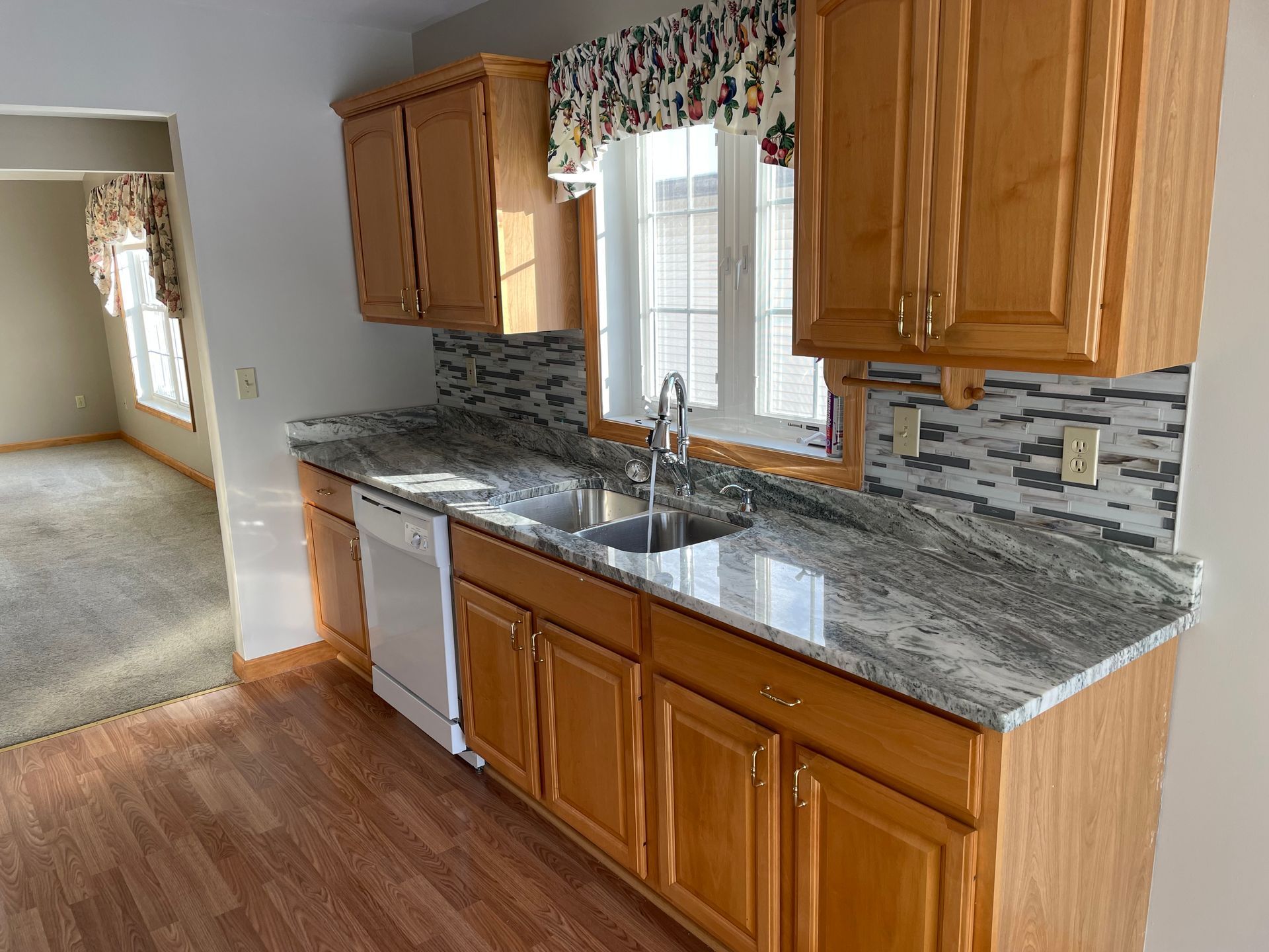 Kitchen with wood cabinets, granite countertops, and backsplash. White dishwasher and sink.
