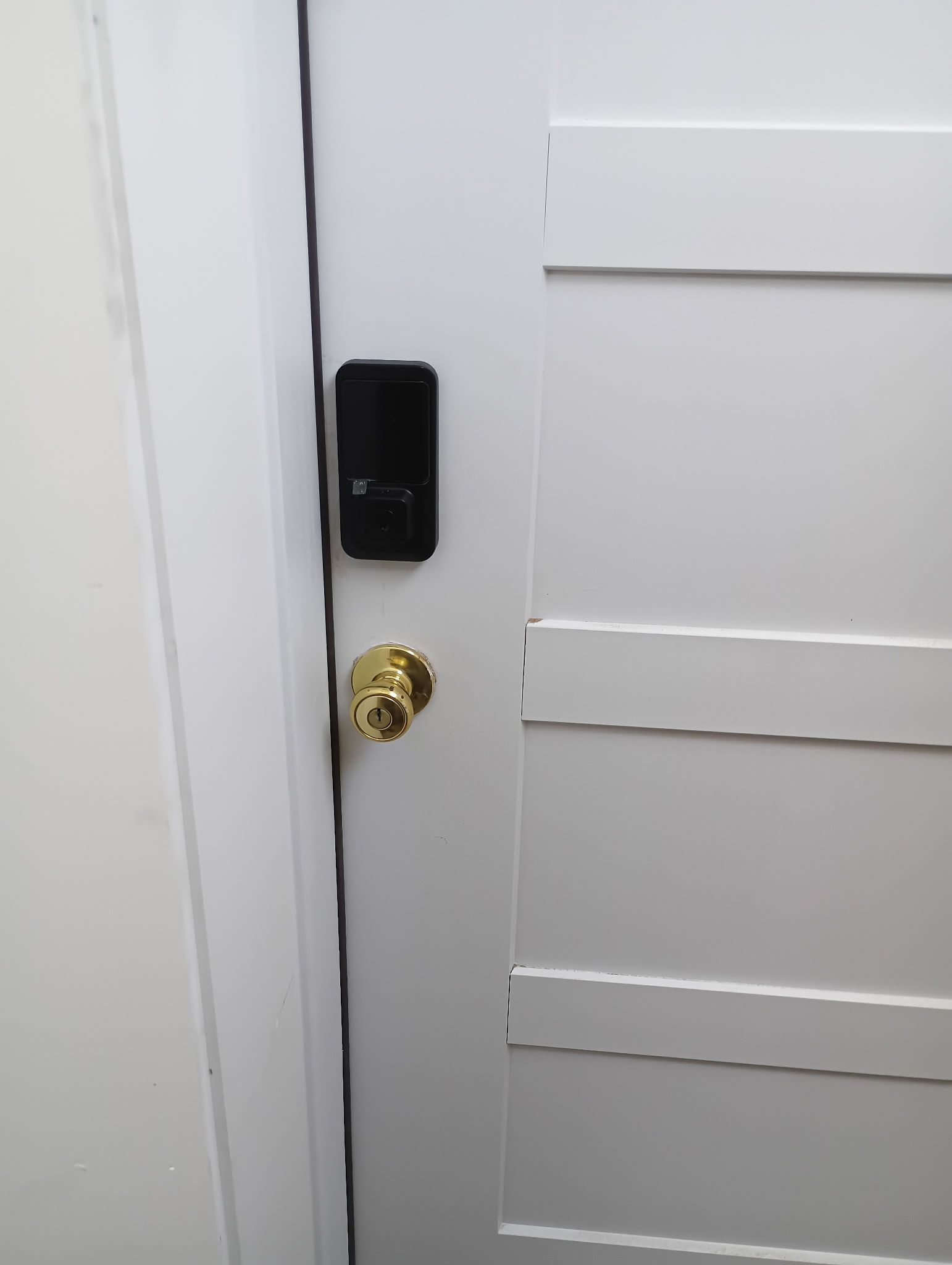 White door with a black smart lock and gold doorknob.