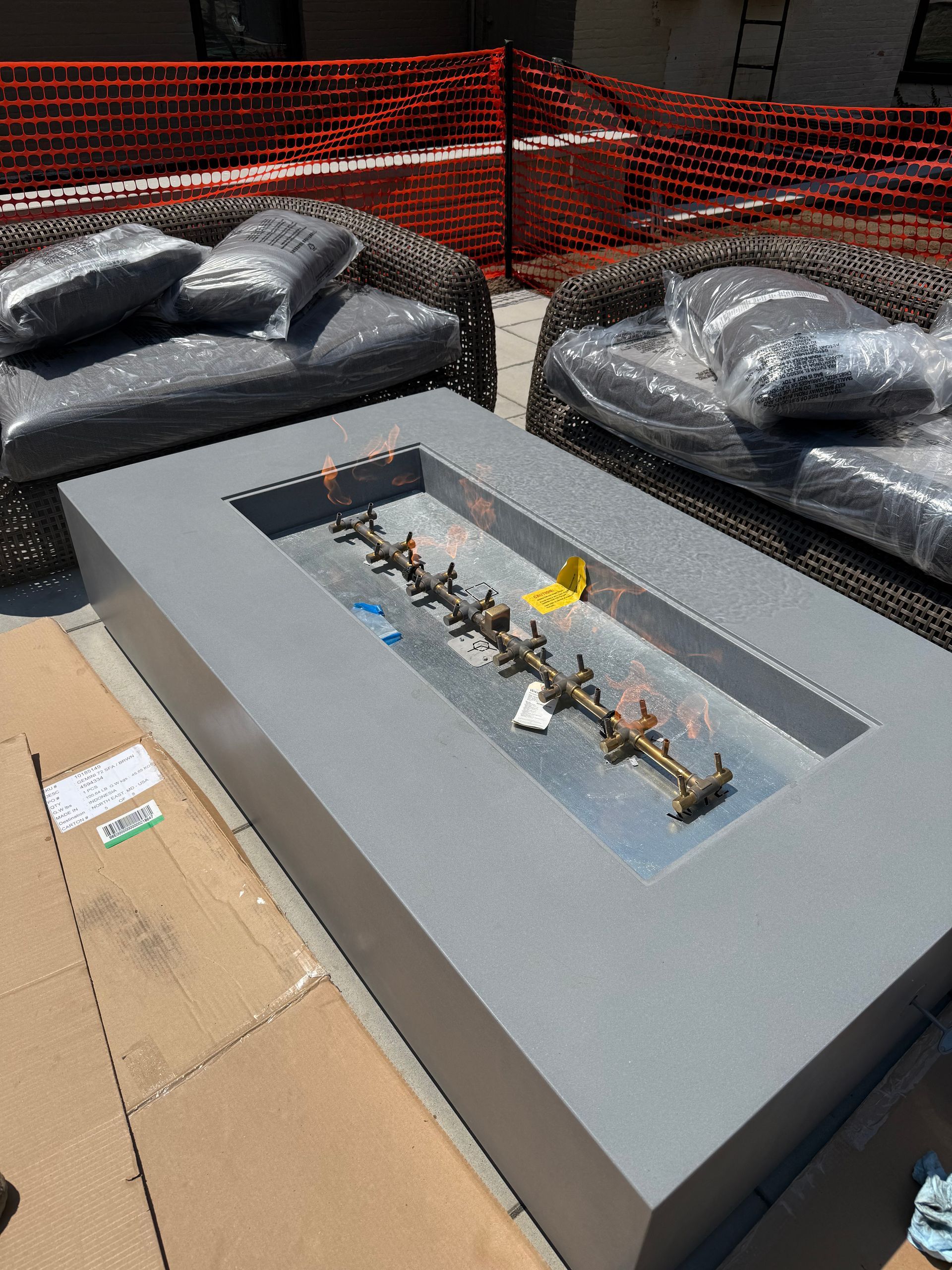 A modern, gray outdoor fire pit with a metal fire feature, flanked by covered wicker seating.