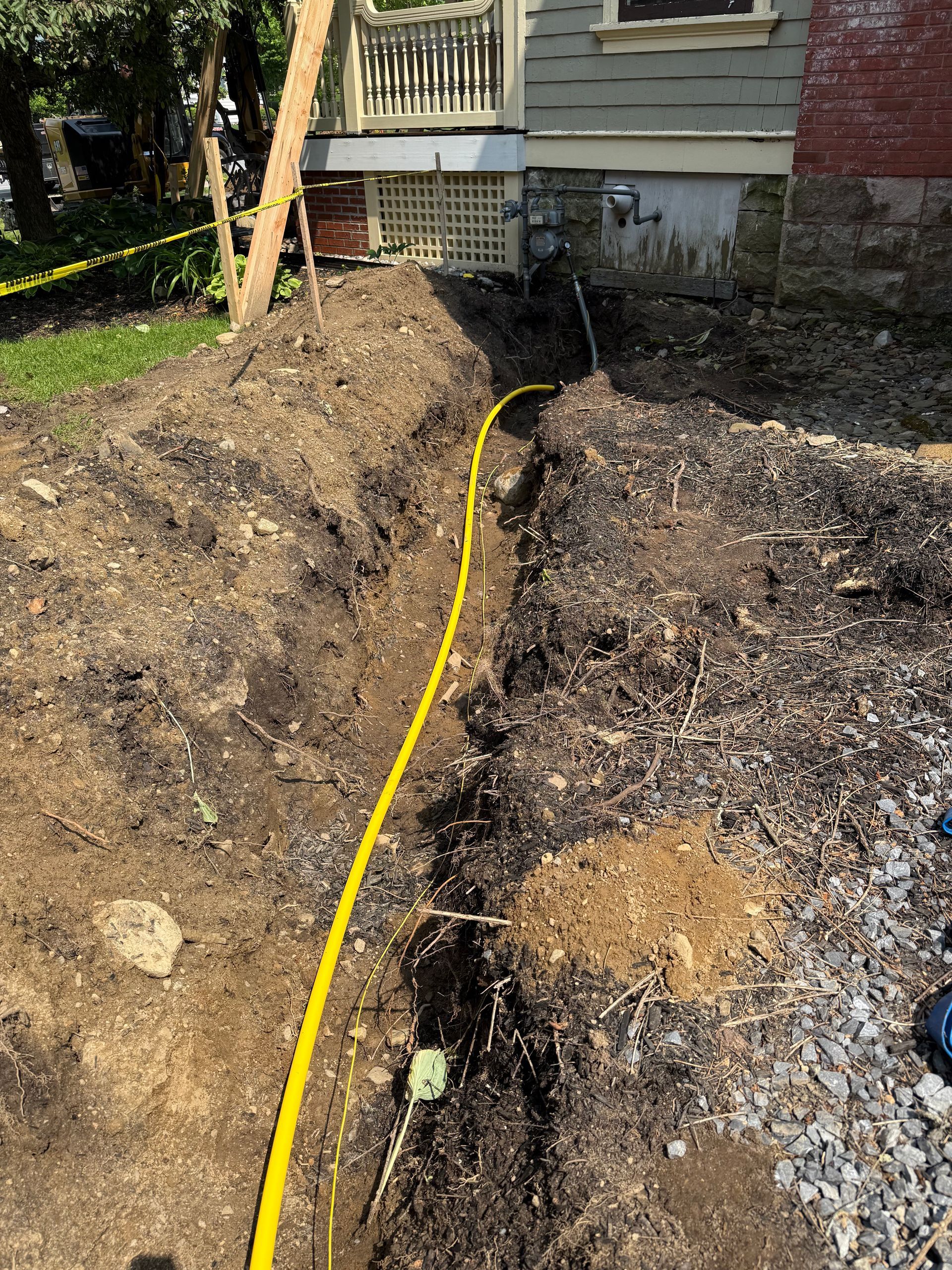 A trench with yellow gas line runs along a house's foundation.