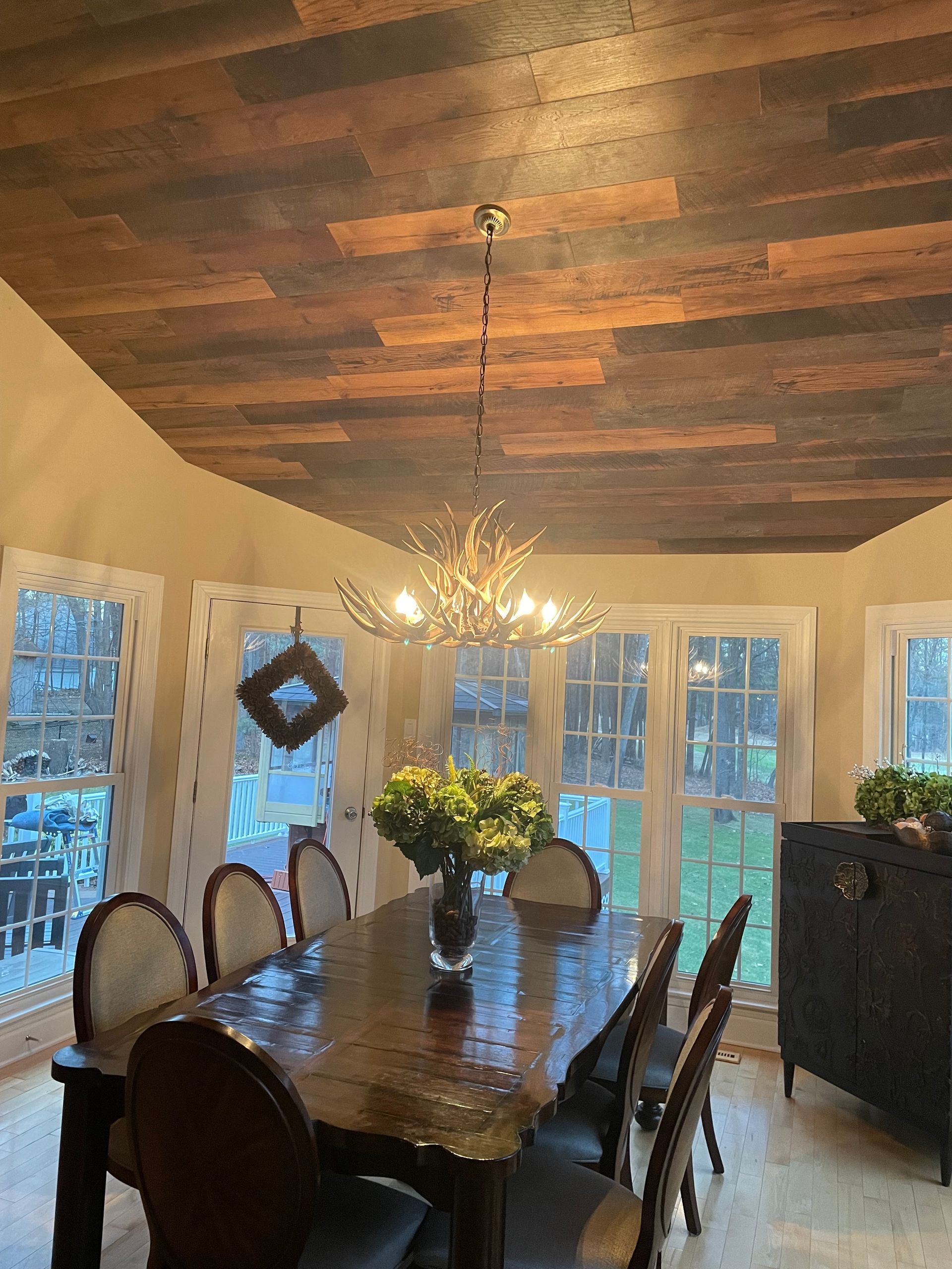 Dining room with wood ceiling, chandelier, dark wooden table, chairs, and windows.