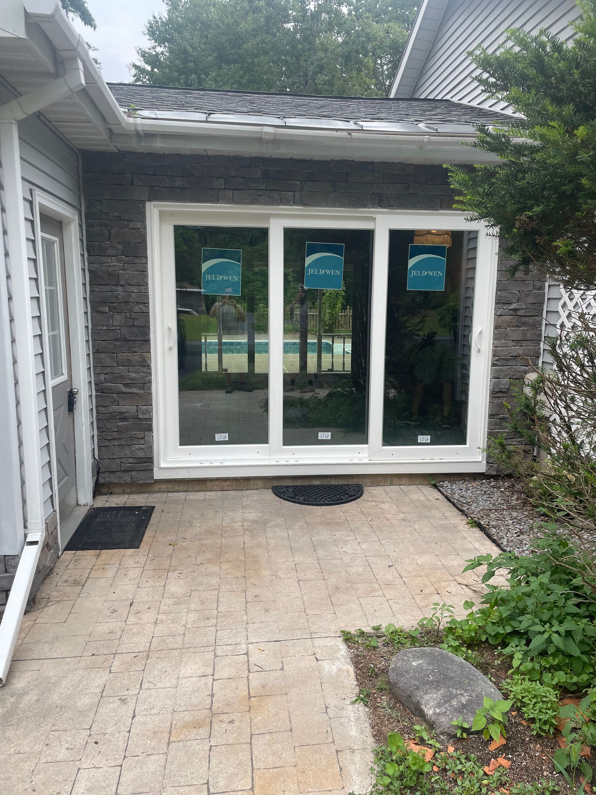 Exterior view: white framed sliding door on stone wall; tan pavers; black welcome mat.