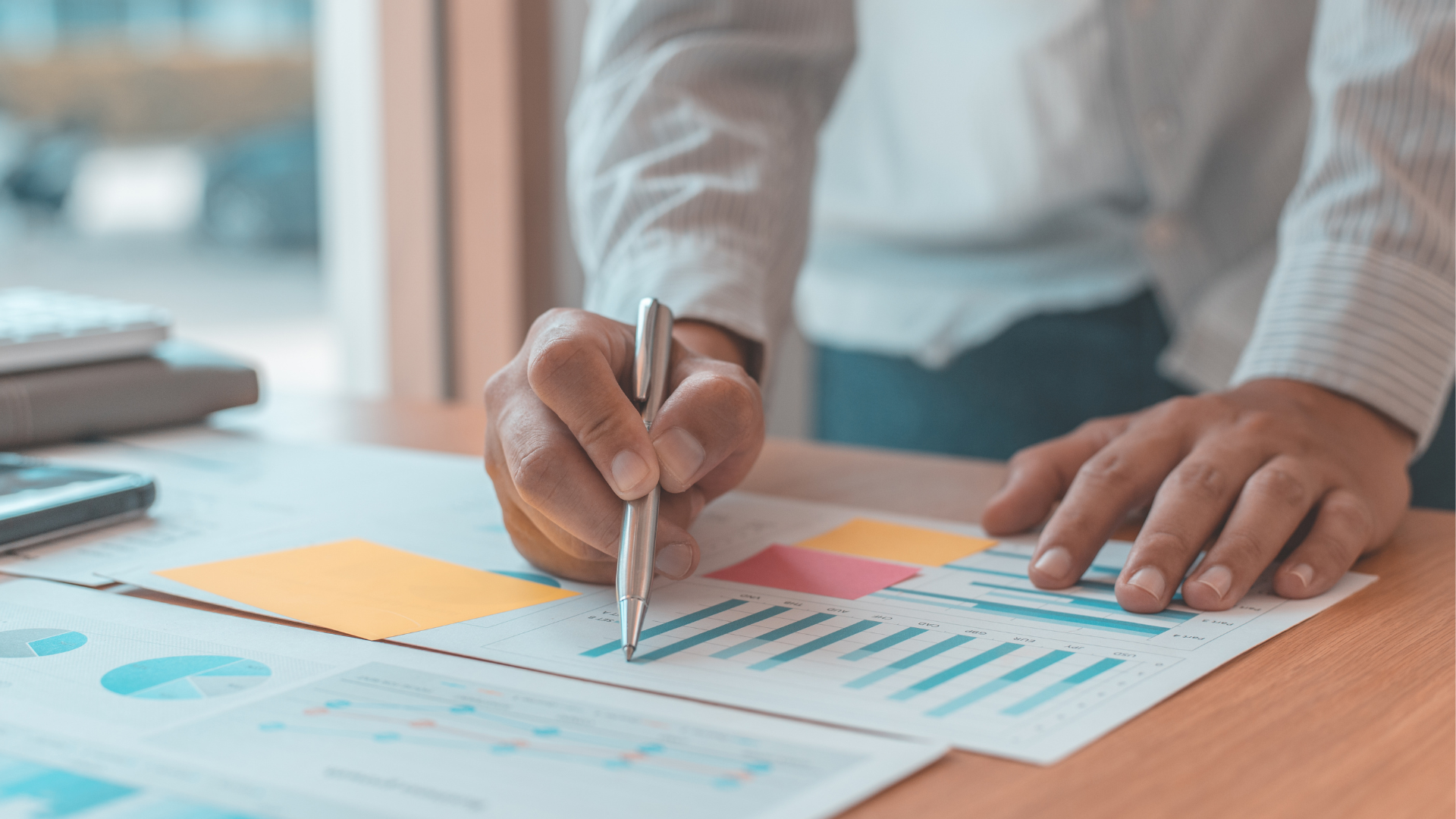 Hands pointing at financial charts on a desk with papers and a pen