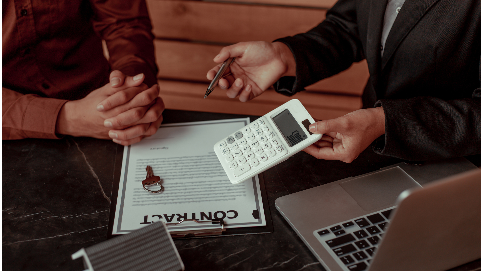 Hands using a calculator over financial papers and a laptop on a desk