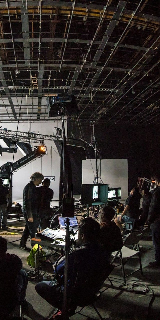 Film set with crew, monitors, lights, and a camera crane. Interior, low light.