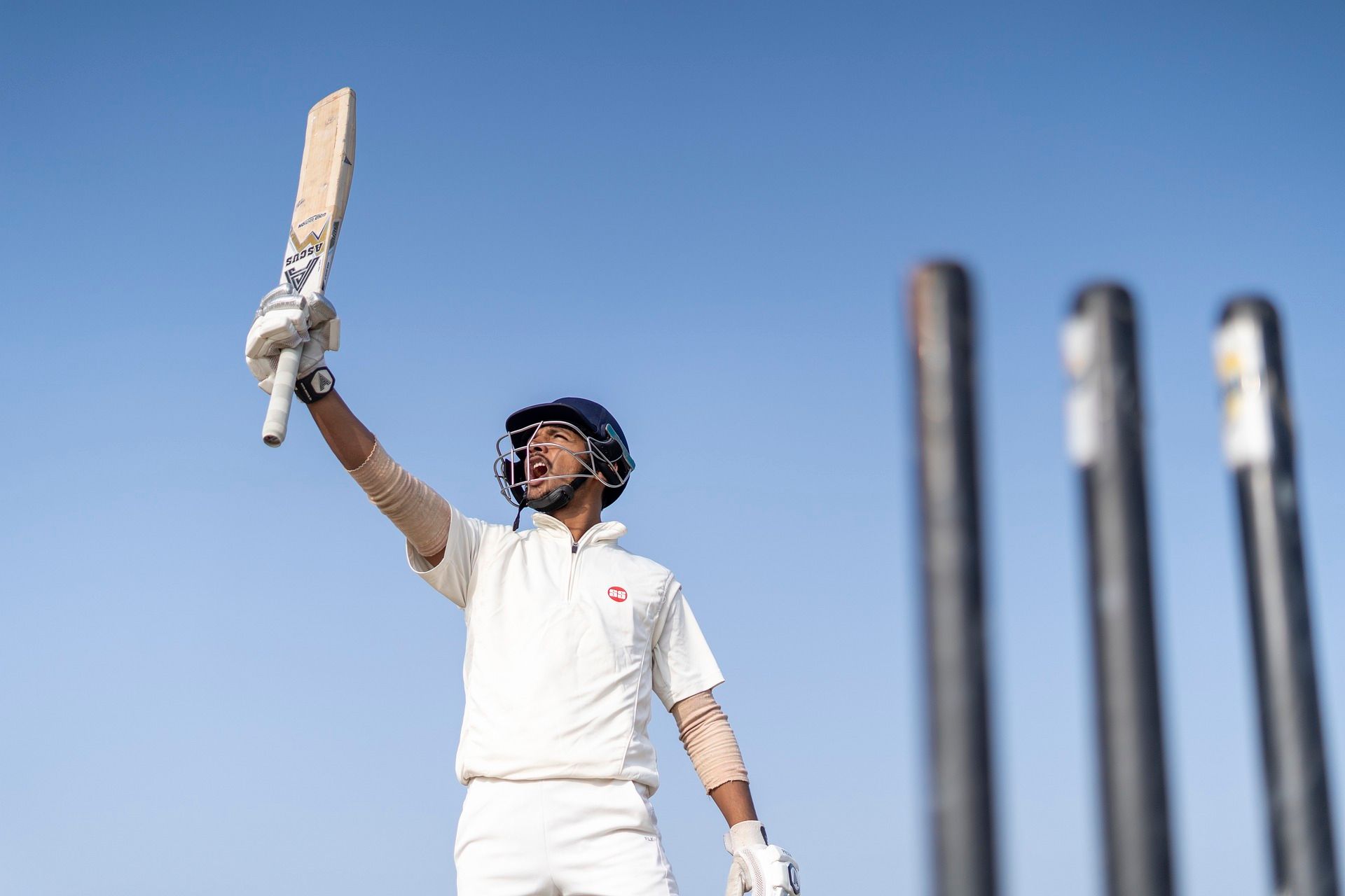 A cricketer is holding a cricket bat in the air.
