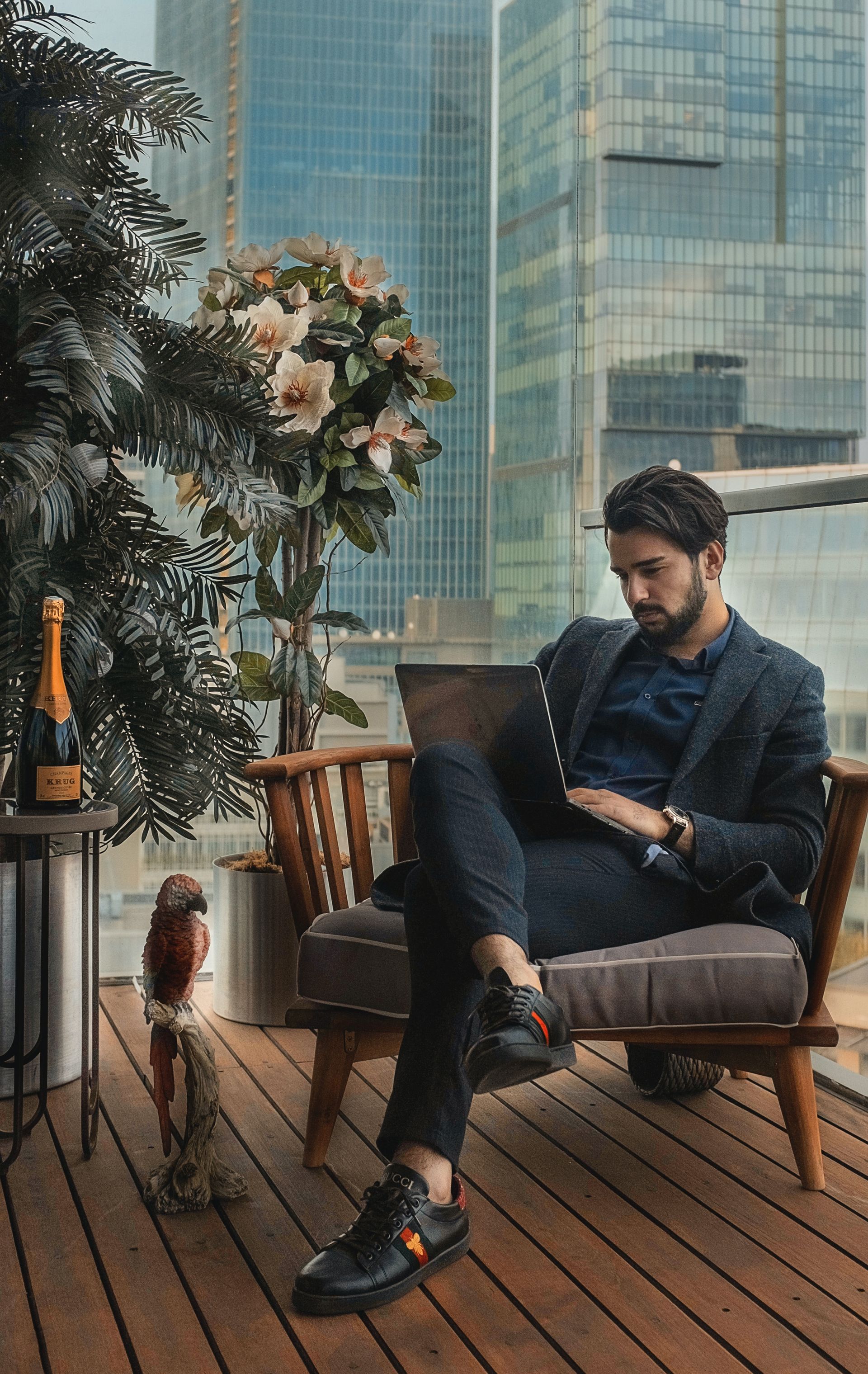 A man in a suit is sitting in a chair on a deck using a laptop.
