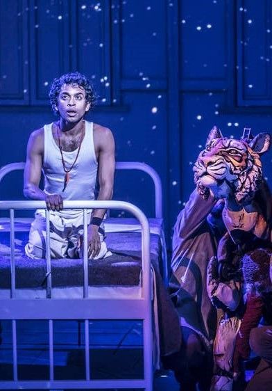 Life of Pi - A man is kneeling on a bed next to a tiger puppet on a stage.